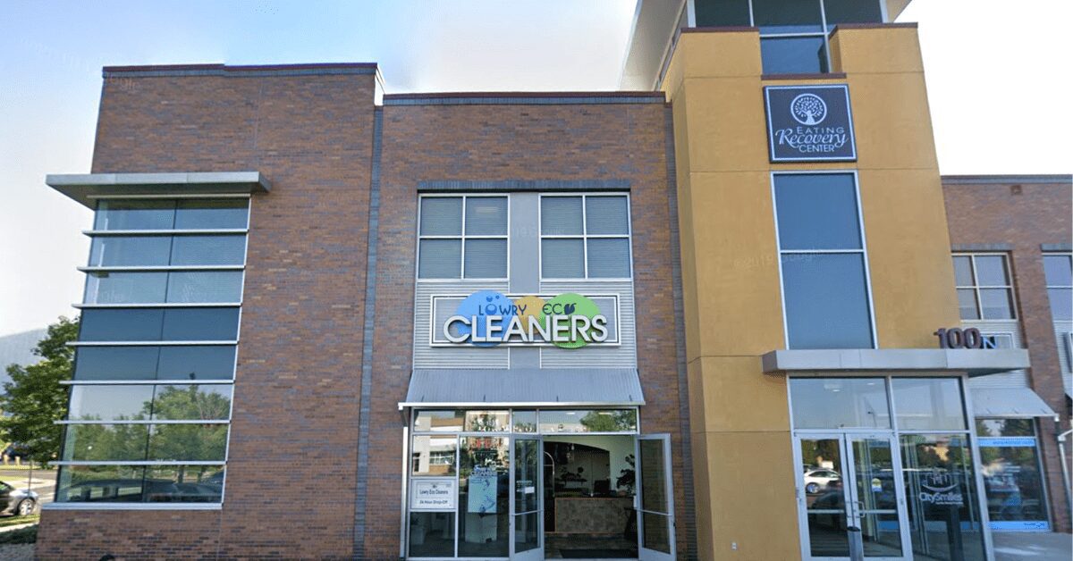 Lowry Eco Cleaners storefront with green and white signage and a large window showcasing clothing items on hangers.