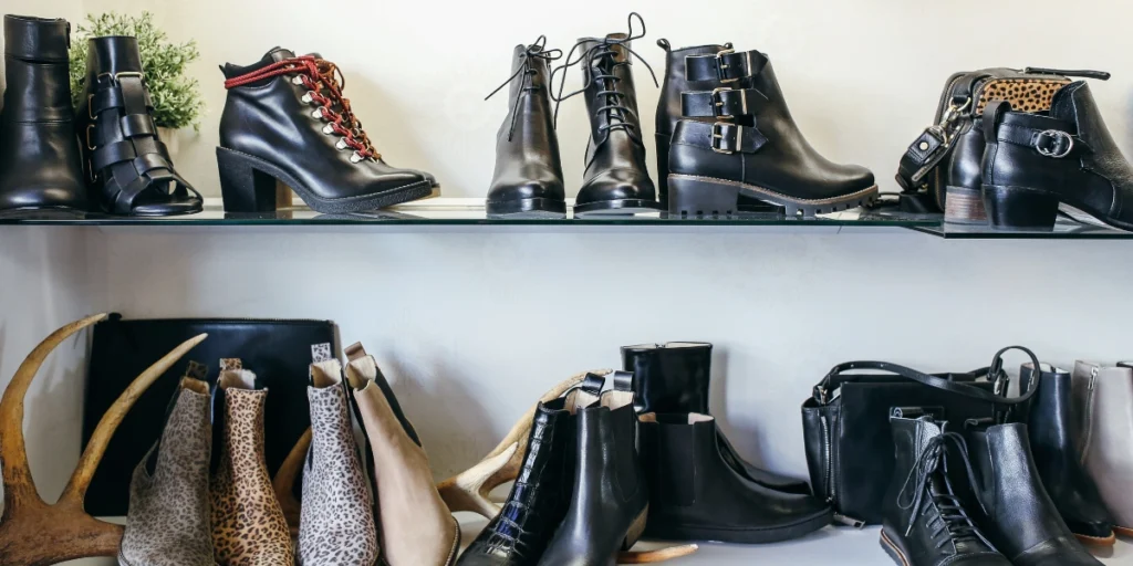 Assorted leather and suede boots and shoes displayed neatly on glass shelves in a boutique or closet setting.